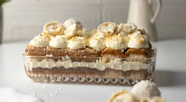 Ein Raffaello Tiramisu in einer Glasform, geschichtet mit Löffelbiskuits, Creme und Kokosraspeln. Obenauf dekorative Kokospralinen.