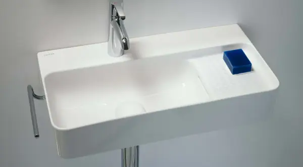 Elegancka, mała umywalka wisząca z chromowaną baterią i kostką niebieskiego mydła.