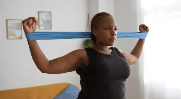 Femme faisant un exercice haut du corps avec un élastique bleu.
