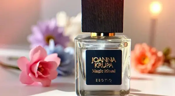 Elegancka butelka perfum Joanna Krupa Magic Ritual na tle kwiatów. Wiele osób szuka magiczne perfumy opinie, by poznać ten zapach.