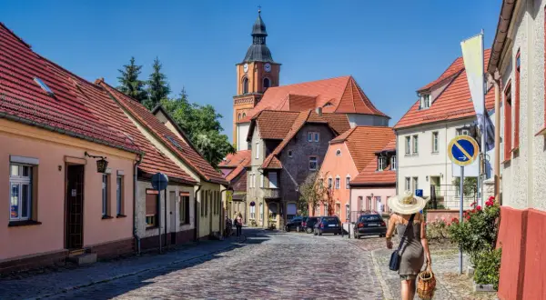 Idyllisches Dorf mit Kopfsteinpflasterstraße, Kirche und einer Frau mit Hut. Perfekt für Ausflugsziele Berlin Brandenburg.