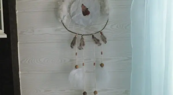 Un attrape rêve, ornement traditionnel, orné d'un loup hurlant, de plumes et de perles, suspendu devant un mur en bois clair.