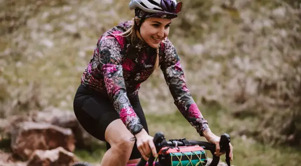 Uśmiechnięta rowerzystka w kwiecistej bluzie pokonuje kolejne kilometry. Dziś czeka ją 50 km na rowerze po malowniczych terenach.
