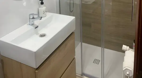 Moderno lavabo sobre mueble de madera, ducha con mampara y azulejos imitación madera. ¡Renovar baño sin obra es posible!