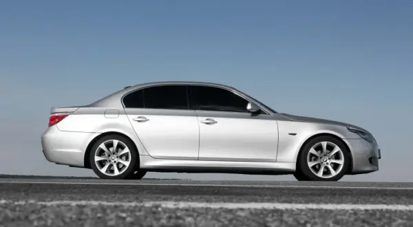 Srebrne BMW 5 E60 na tle błękitnego nieba, zaparkowane na drodze.