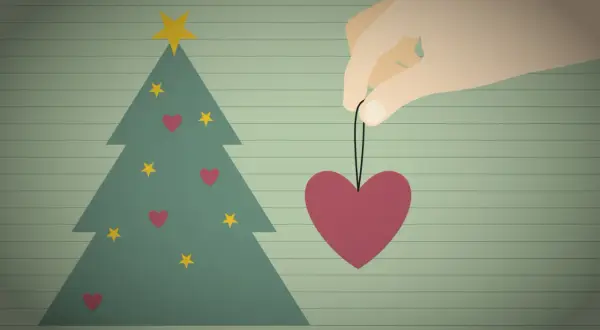Ein Herz als Weihnachtsbaumschmuck, gehalten von einer Hand, symbolisiert eine besinnliche Weihnacht voller Liebe.