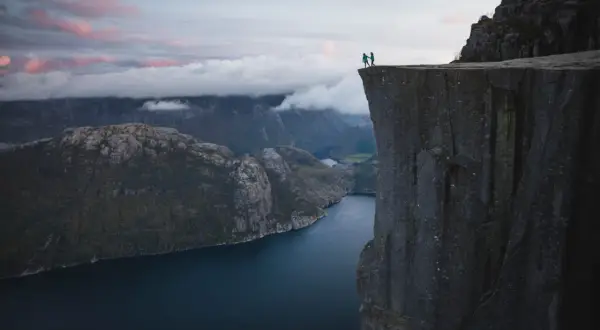 Två personer står på en klippavsats med hisnande utsikt över en fjord. Trots **höjdrädsla** vågar de sig nära kanten.