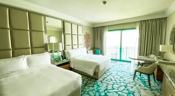 Pokój hotelowy z dwoma łóżkami, widokiem na balkon i ocean. Zastanawiasz się, ile kosztuje doba w hotelu?