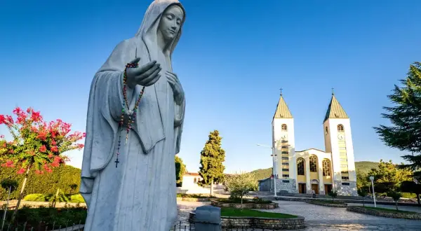 Pomnik Matki Bożej z różańcem przed kościołem w Medziugorie. Planujesz podróż? Dowiedz się, jak dolecieć samolotem do Medziugorie.