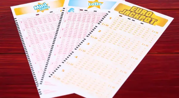 Kupony lotto: Mini Lotto, Lotto Plus i Eurojackpot na drewnianym tle.