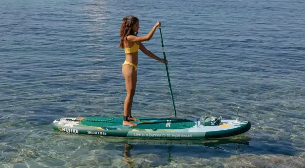 Woman in yellow bikini paddleboarding on a calm, clear sea.