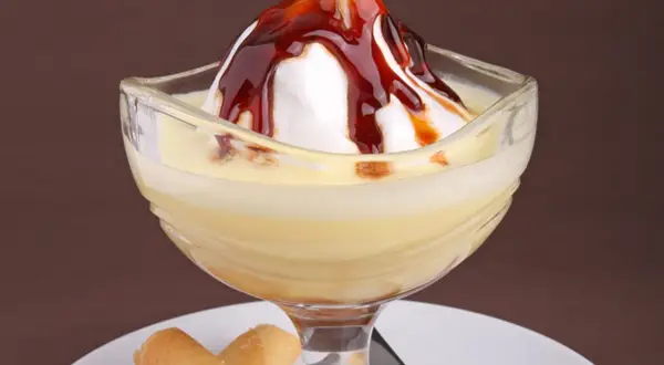 Un dessert crémeux avec une meringue nappée de caramel, servi dans un verre, évoquant des iles flottantes. Des biscuits fins l'accompagnent.