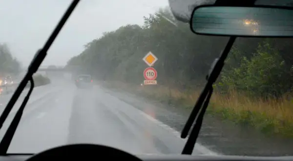 Conduire sous la pluie sur une route mouillée, avec des essuie-glaces en action et un panneau de rappel de vitesse 110.