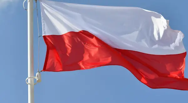 Biało-czerwona bandera flaga Polski powiewa na maszcie na tle błękitnego nieba.