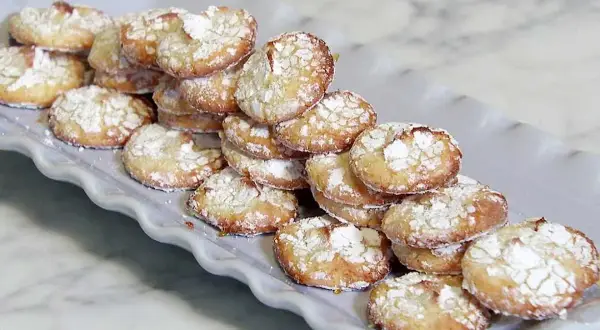 En hög med hembakade amaretti-kakor, pudrade med florsocker, redo att avnjutas. Ett enkelt amaretti recept.