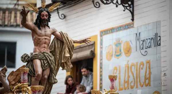 Imagen de una escultura de Cristo en una procesión de Martes Santo. La figura, con corona de espinas dorada, porta una túnica dorada y levanta una mano.