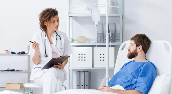 Lekarka omawia z pacjentem potencjalne immunoterapia skutki uboczne. Pacjent leży w łóżku szpitalnym, podłączony do kroplówki.