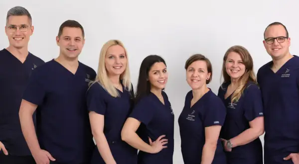 Grupa uśmiechniętych dentystów w granatowych uniformach na białym tle.