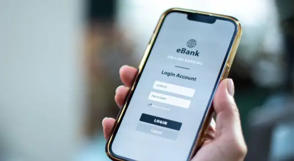 Dłoń trzyma smartfon z ekranem logowania do bankowości internetowej. Ktoś zapłacił moją kartą przez internet, muszę to sprawdzić.