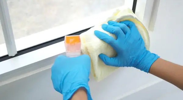 Ręce w niebieskich rękawiczkach czyszczą białe ramy okienne plastikowe. Użyj delikatnego środka do czyszczenia, by przywrócić im blask.