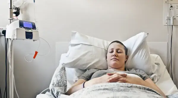 Kobieta zmagająca się z rakiem piersi z przerzutami odpoczywa w szpitalnym łóżku, podłączona do pompy infuzyjnej.