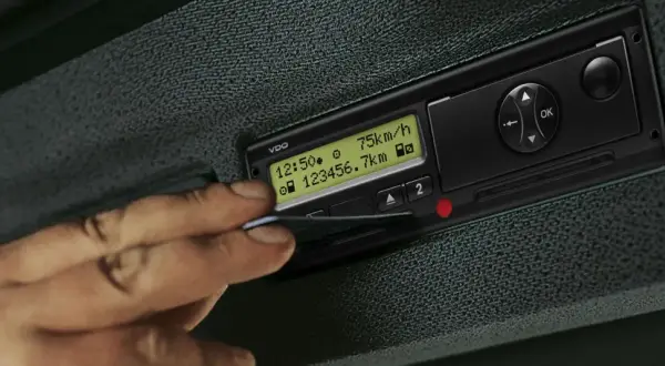 Une main insère une carte dans un tachygraphe intelligent VDO affichant 75 km/h et 23456.7 km.