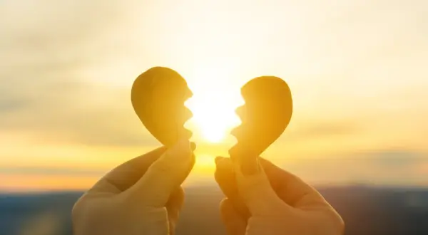 Mani che tengono due pezzi di un cuore spezzato contro un tramonto dorato. Un sentimento di nostalgia, non riesco a lasciarti andare.