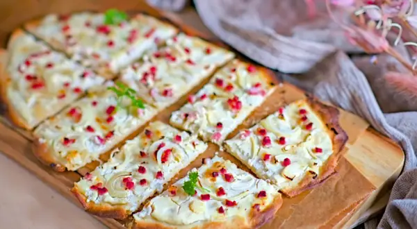 Flammkuchen mit cremigem Belag, Zwiebeln und roten Speckwürfeln. Ein köstlicher Flammkuchen Belag, der Appetit macht.