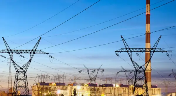 Elektrownia z kominem i liniami wysokiego napięcia. W tle widać budynki zakładu, a nad nimi niebo o zmierzchu. To obraz, który może kojarzyć się z opłatą kogeneracyjną.