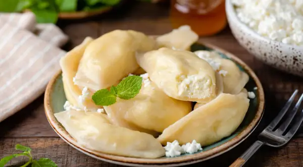 Pyszne pierogi z serem na słodko, udekorowane miętą i twarożkiem. Idealne na deser lub śniadanie.
