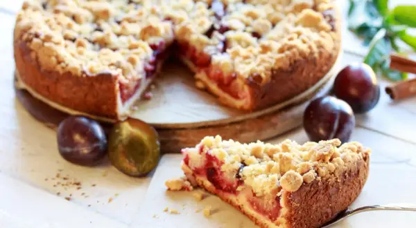 Saftiger Pflaumenkuchen mit Streuseln, perfekt für ein leckeres Pflaumenkuchen Rezept. Frische Pflaumen und Zimt daneben.