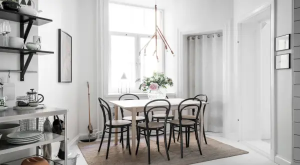 En ljus och mysig matplats med ett träbord, svarta stolar och en vacker blomsterbukett. En taklampa i trä ger ett varmt sken.