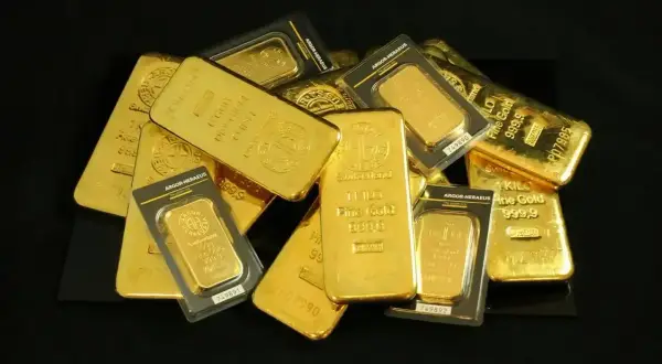 Kupa błyszczących sztabek złota, każda o charakterystycznym, lśniącym połysku. Widać napisy "Fine Gold 999,9" i "1 KILO", które pokazują, jak wygląda złoto w swojej najczystszej formie.