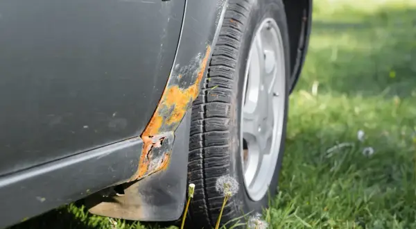 Widoczna rdza pod lakierem na progu samochodu, obok opony i zielonej trawy.