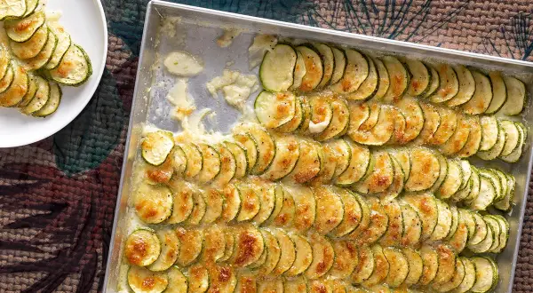 Fette di zucchine al forno con mozzarella filante, disposte in file ordinate in una teglia, pronte per essere gustate.