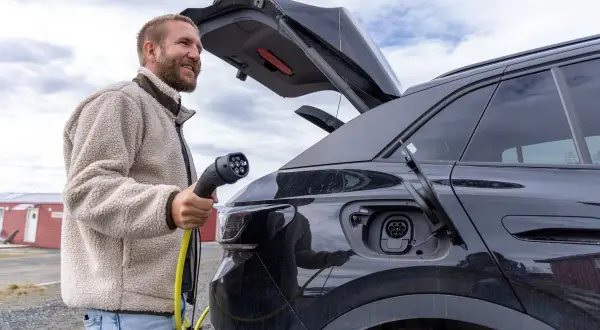 Man laddar sin soc elbil utomhus. En gul laddkabel hänger från bilen.