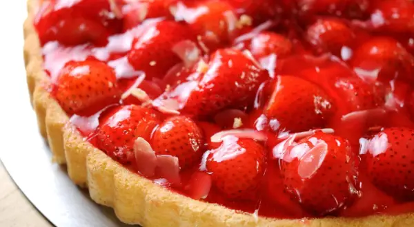 Una deliziosa torta di fragole, con fragole fresche e succose ricoperte da una lucida glassa rossa, su una base dorata.