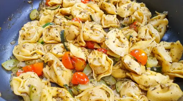 Pyszne tortellini z serem, podsmażane z cukinią i pomidorkami koktajlowymi, doprawione ziołami.
