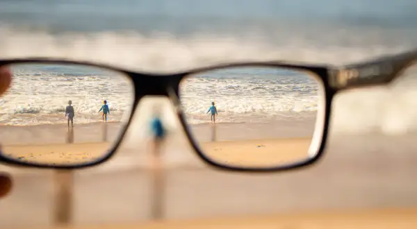 Okulary korygujące widzenie na plaży z dwojgiem dzieci w tle.