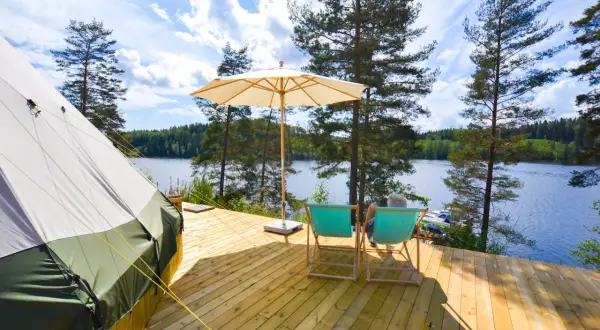 En glampingtält och två solstolar på en träaltan vid en sjö. En perfekt plats att koppla av på Råå Vallar Resort.
