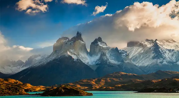 Majestatyczne szczyty Torres del Paine w **Tierra del Fuego** oświetlone słońcem, z turkusowym jeziorem u podnóża.