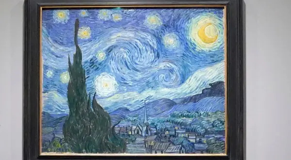 Van Gogh's blaues Bild zeigt einen wirbelnden Sternenhimmel über einem Dorf. Zypressen ragen empor, Sterne leuchten, der Mond strahlt.