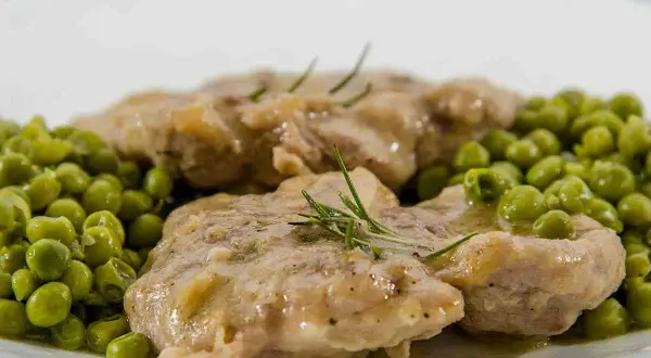Ossobuco con piselli, un piatto succulento con carne tenera e piselli freschi, guarnito con rosmarino.