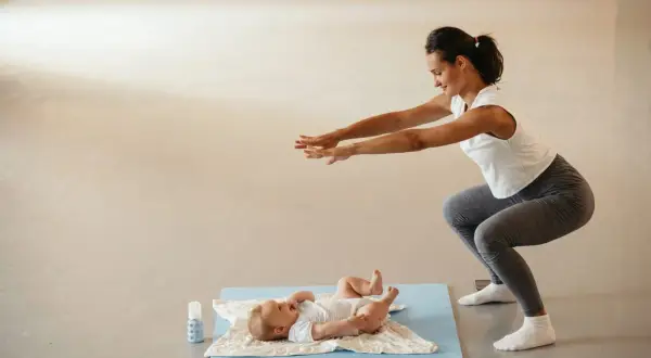 Madre haciendo sentadillas con su bebé cerca, un ejemplo de deporte postparto.