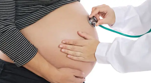 Une sage-femme utilise un stéthoscope pour le monitoring d'un ventre de femme enceinte.