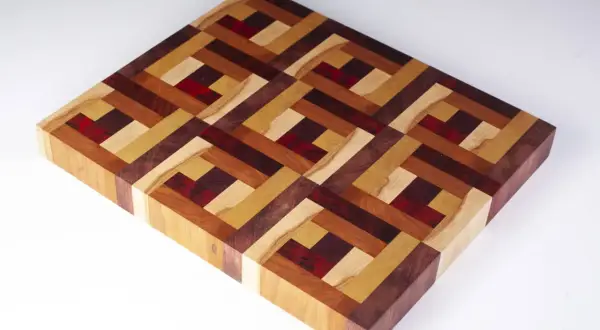 A beautiful diy cutting board with an intricate geometric pattern made from various wood types and red accents.