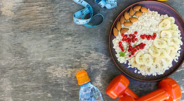 Zdrowa dieta na redukcję: owsianka z owocami, migdały, woda i hantle. Idealny zestaw na początek dnia.
