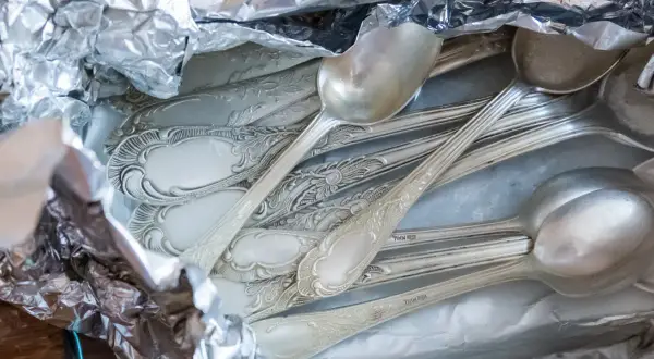 Stos srebrnych łyżek i widelców owiniętych w folię aluminiową.