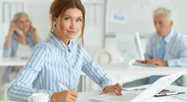 Kobieta w biurze, pracująca przy laptopie. Jej kod zawodu to księgowa, która skrupulatnie wypełnia dokumenty.