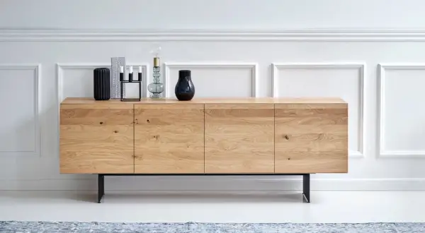 Ett stilrent sideboard i ljust trä med svarta ben, dekorerat med vaser och ljusstakar.